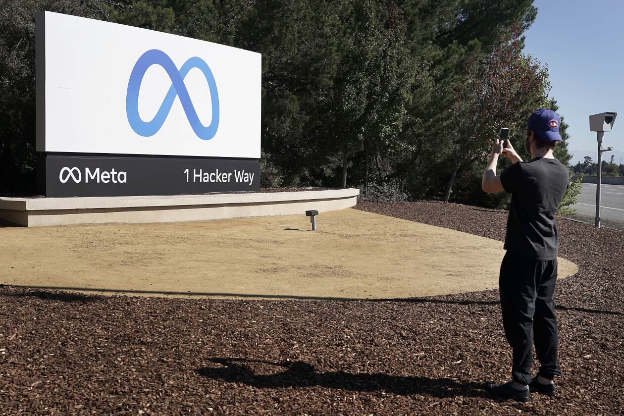 A Facebook employee takes a photo in front of the new Meta Platforms Inc. sign outside company headquarters in Menlo Park, Calif.